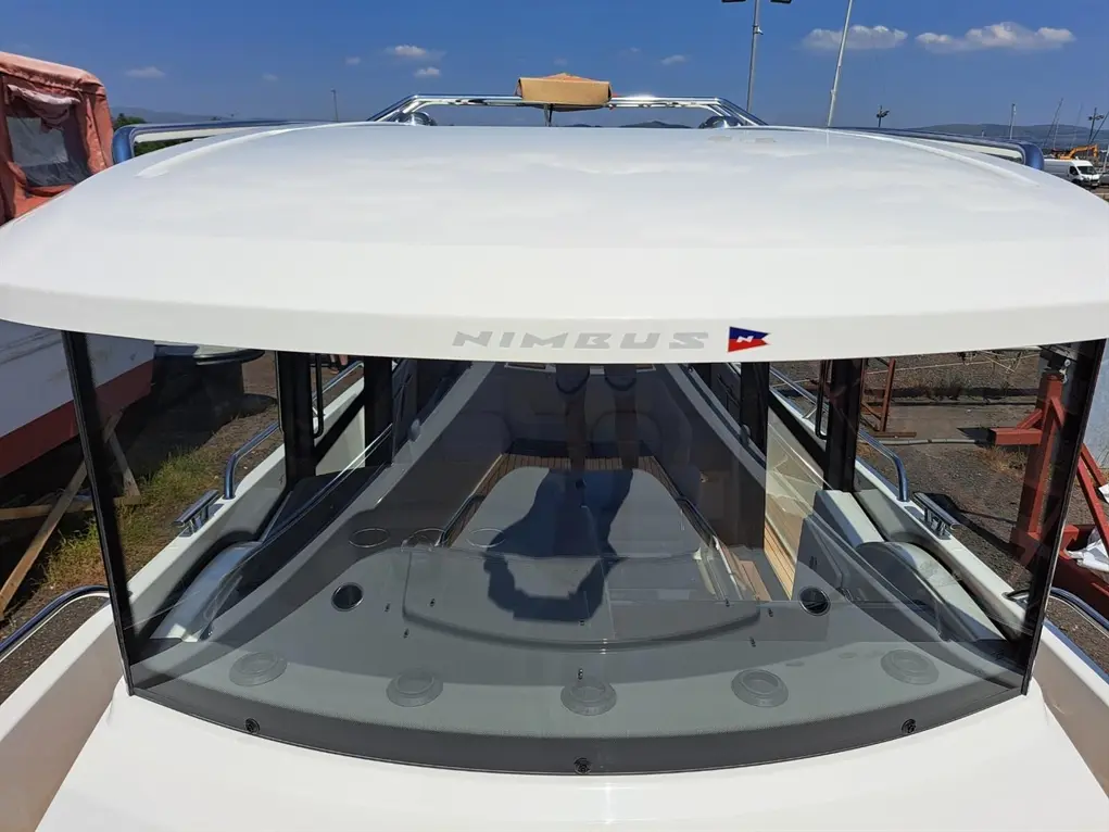 View of a Nimbus boat's top with a sleek white roof and large windshield, showcasing the deck layout and marine environment.